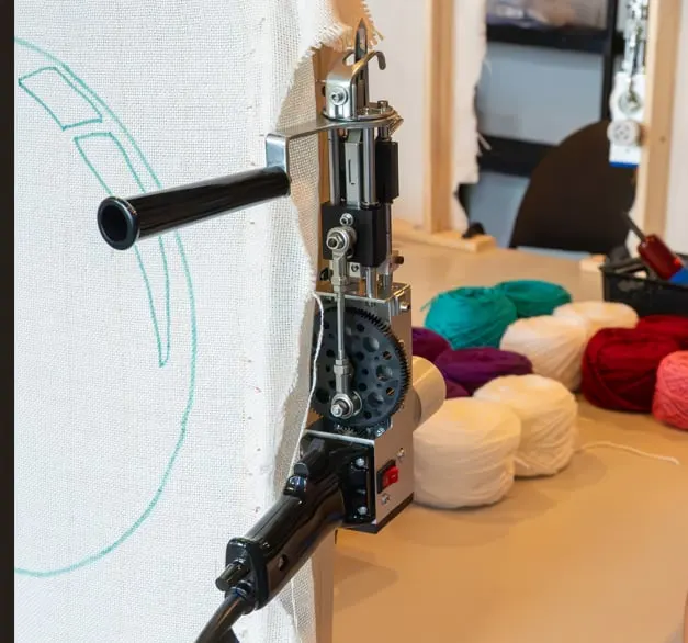 Pistolet à tufting monté sur un cadre, devant le mur de laine